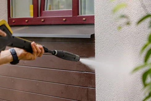 Person reinigt Hauswand mit Hochdruckreiniger